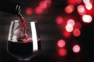 Pouring red wine into glass against dark background with blurred lights, closeup.