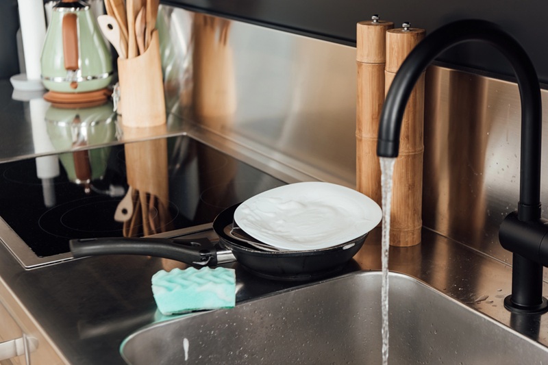 Selective focus of plate, frying pan and sponge in soap near kitchen