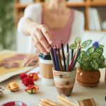 Creative woman taking colored pencil from holder while sitting