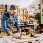 Handsome carpenter in goggles holding pencil in carpentry shed