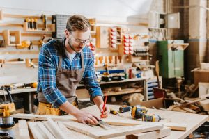 Handsome carpenter in goggles holding pencil in carpentry shed
