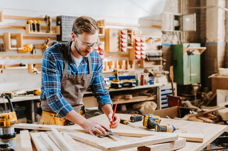 Handsome carpenter in goggles holding pencil in carpentry shed Handsome carpenter in goggles holding pencil in carpentry shed