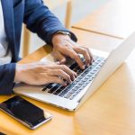Young man, wearing glasses and smiling, as he works on his laptop