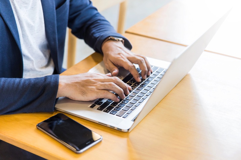 Young man, wearing glasses and smiling, as he works on his laptop