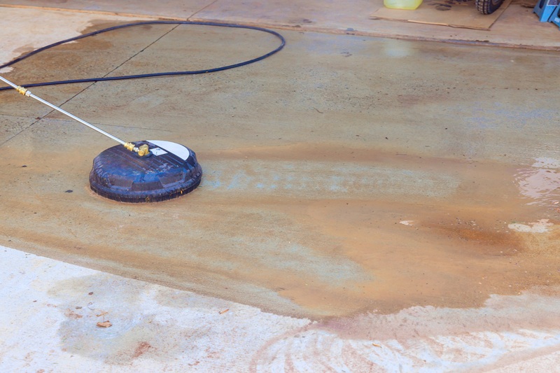 Person is pressure washing stained garage floor, spraying awa