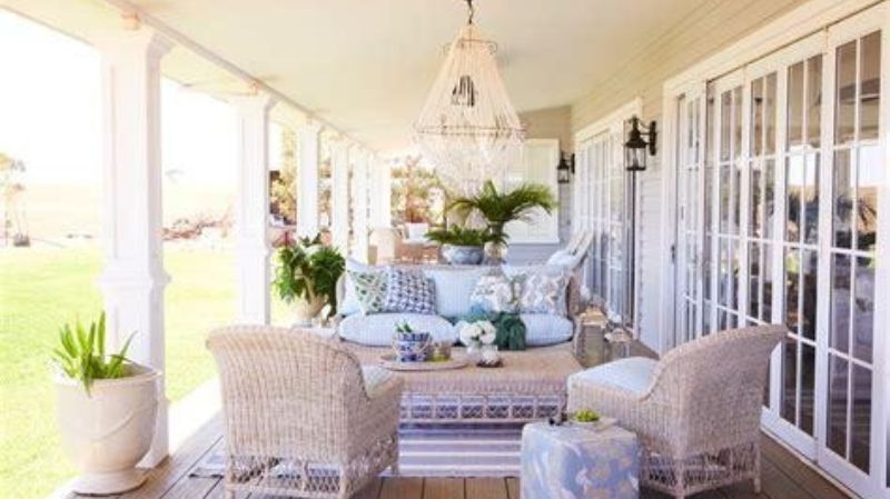 A cozy covered porch with white wicker furniture, plants, and a chandelier
