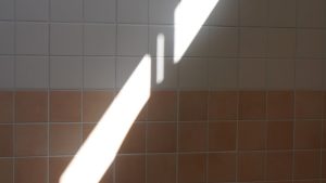 Diagonal sunlight strikes a tiled wall in a sharp geometric pattern