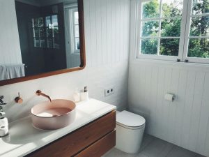 Modern bathroom featuring white shiplap walls, a wooden vanity, and a pink vessel sink