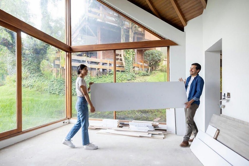 Two people are carrying a large white board while renovating