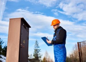 Worker takes notes on a clipboard while inspecting an outdoor utility box