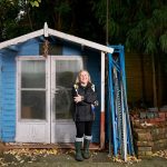 A Woman in Black Jacket Standing In Front of a Blue Shed