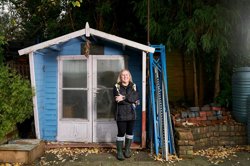 A Woman in Black Jacket Standing In Front of a Blue Shed