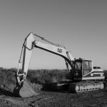 A black and white photograph captures a CAT 320L excavator stationary on a construction site