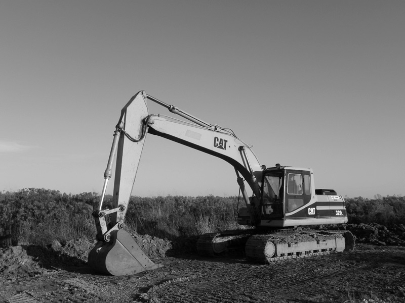 A black and white photograph captures a CAT 320L excavator stationary on a construction site