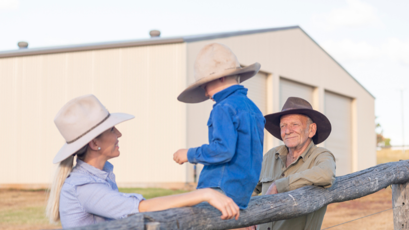 Family standing by a fence in front of a rural steel shed in Australia, highlighting lifestyle and steel sheds Australia use