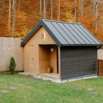 Wooden cabin standing in a green backyard with autumn trees in the background
