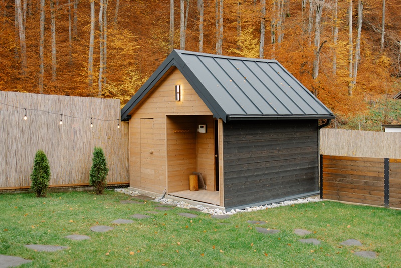 Wooden cabin standing in a green backyard with autumn trees in the background