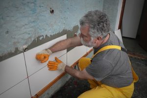 Worker placing ceramic tile to wall in bathroom