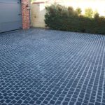 a large, professional cobblestone driveway leading up to a modern grey garage