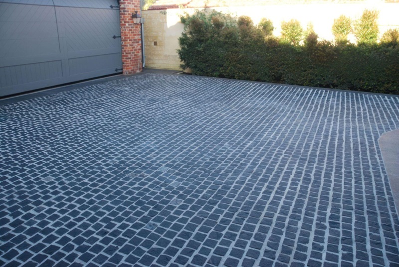 a large, professional cobblestone driveway leading up to a modern grey garage