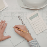 Architect reviewing blueprints with a notepad and laptop nearby
