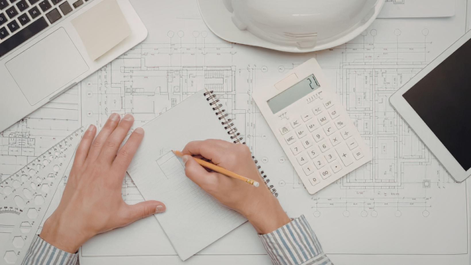 Architect reviewing blueprints with a notepad and laptop nearby Architect reviewing blueprints with a notepad and laptop nearby