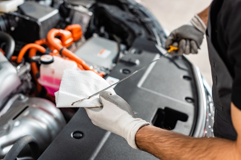 Mechanic wearing gloves inspecting the engine bay while holding a paper towel and a tool.