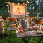 Outdoor backyard movie night with a projector screen, string lights, and rustic seating with snacks and drinks.