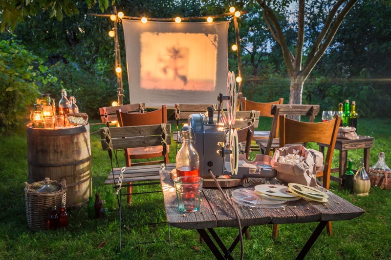 Open air cinema with retro projector in backyard Outdoor backyard movie night with a projector screen, string lights, and rustic seating with snacks and drinks.