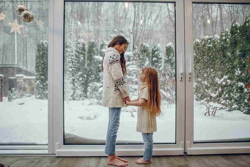 Sisters Holding Hands by Large Glass Patio Door