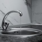 Chrome kitchen faucet pouring a thin stream into a round stainless steel sink on a dark countertop with marble backsplash (monochrome). In-use image showing running water into a basin.