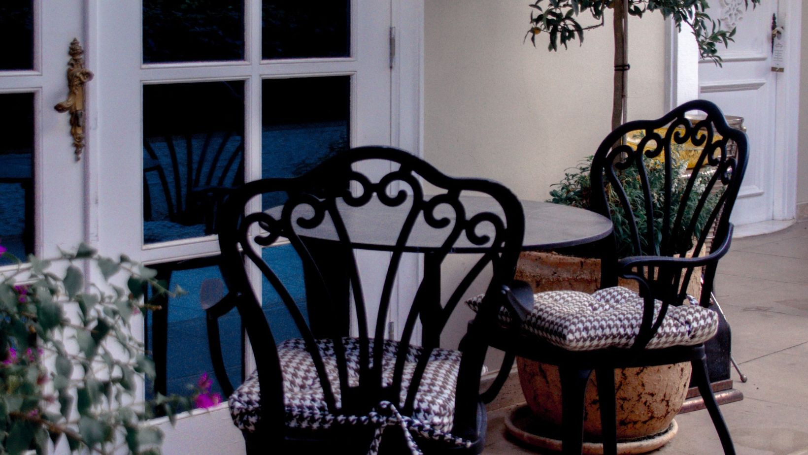 Elegant outdoor patio with vintage wrought iron chairs, potted plants, and decorative doorway. Elegant outdoor patio with vintage wrought iron chairs, potted plants, and decorative doorway.