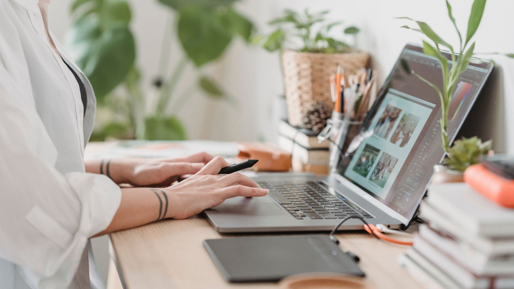 Freelance designer working from home using a laptop and digital tablet, surrounded by plants