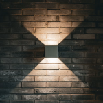 A square wall light on a brick wall casting an X-shaped glow on the bricks.