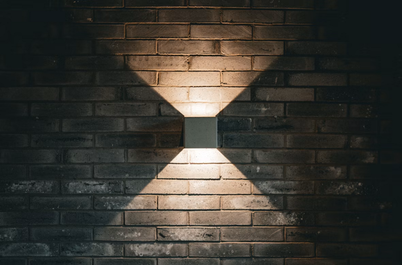 A square wall light on a brick wall casting an X-shaped glow on the bricks.