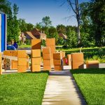 Moving truck parked on a suburban street with stacked cardboard boxes along the sidewalk.