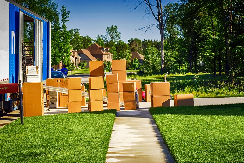 Moving truck parked on a suburban street with stacked cardboard boxes along the sidewalk.