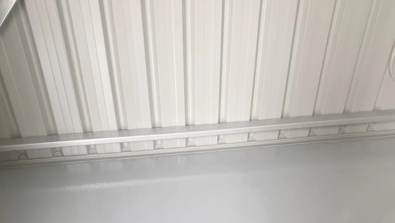 White corrugated metal ceiling with vertical ribs and a horizontal support rail visible across the lower portion of the image