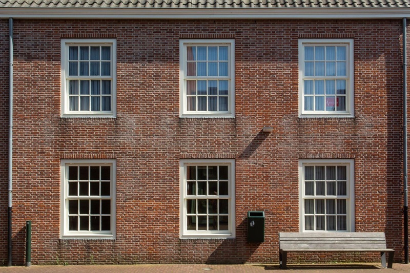 Brick building facade with six white-framed sash windows (three on each floor), a green mailbox, and a wooden bench in front.