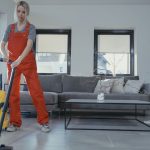 Two women in red overalls vacuuming and sweeping a modern living room