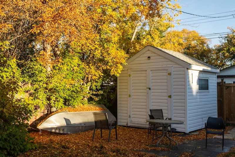 White Backyard Storage Shed in Autumn Landscape White Backyard Storage Shed in Autumn Landscape