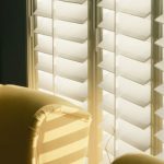 Sunlit yellow striped chair bathed in light as white plantation shutters cast shadows nearby.
