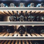 A modern wine cellar with neatly arranged wine racks and a visible climate-controlled cooling system.