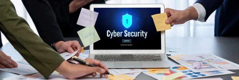 Analyst team use sticky note for creative brainstorm with BI data. Prodigy Team meeting around a laptop showing a Cyber Security screen with a shield icon and scattered sticky notes and documents.