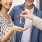 Smiling couple receives a key from another person, symbolizing a new home or move-in moment.