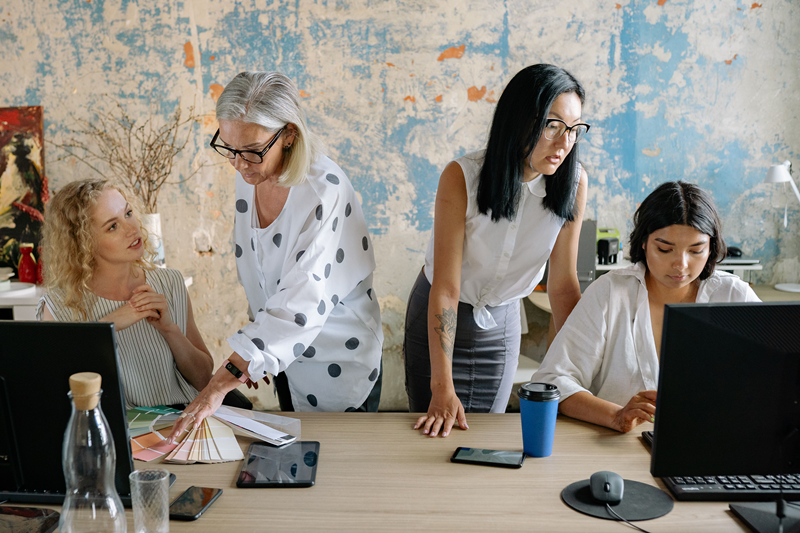 Four diverse women engaged in creative teamwork at a stylish office space, working collaboratively Four diverse women engaged in creative teamwork at a stylish office space, working collaboratively
