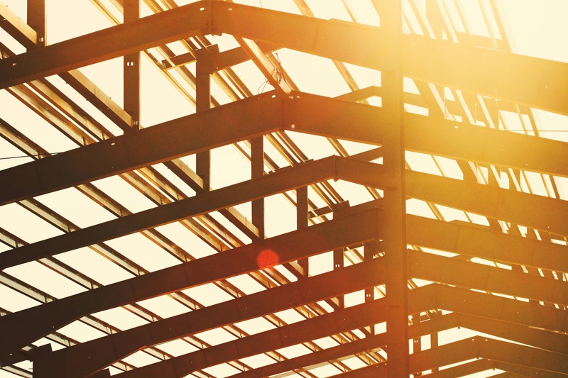 Golden sunlight bathes a steel frame under construction, with intersecting beams forming a grid.