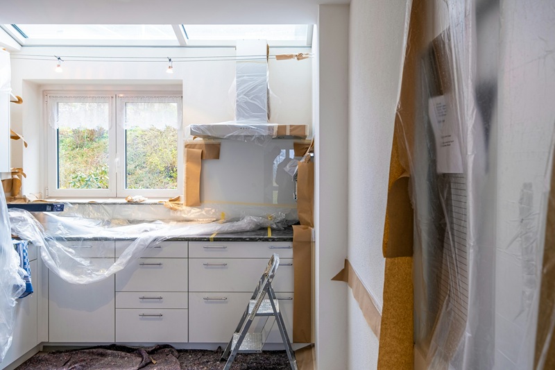 A kitchen under renovation with white cabinets covered in plastic and brown paper A kitchen under renovation with white cabinets covered in plastic and brown paper