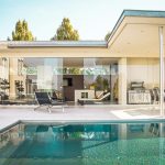 A modern house with glass walls beside a swimming pool on a sunny day