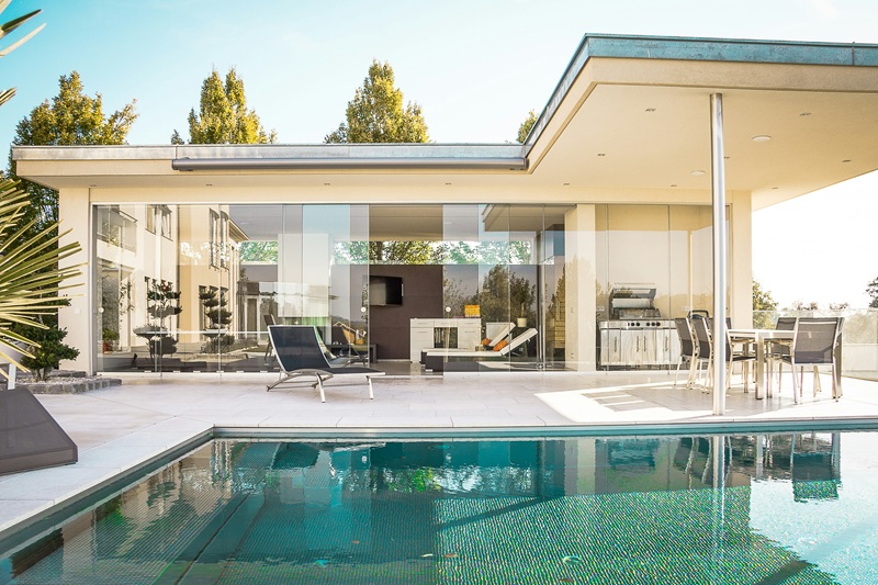 A modern house with glass walls beside a swimming pool on a sunny day A modern house with glass walls beside a swimming pool on a sunny day